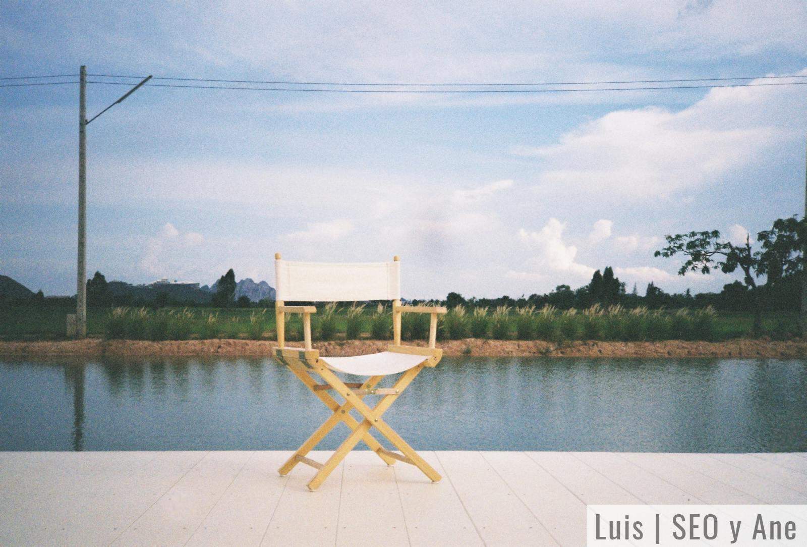 A solitary director's chair on a wooden platform beside a serene river and lush landscape.